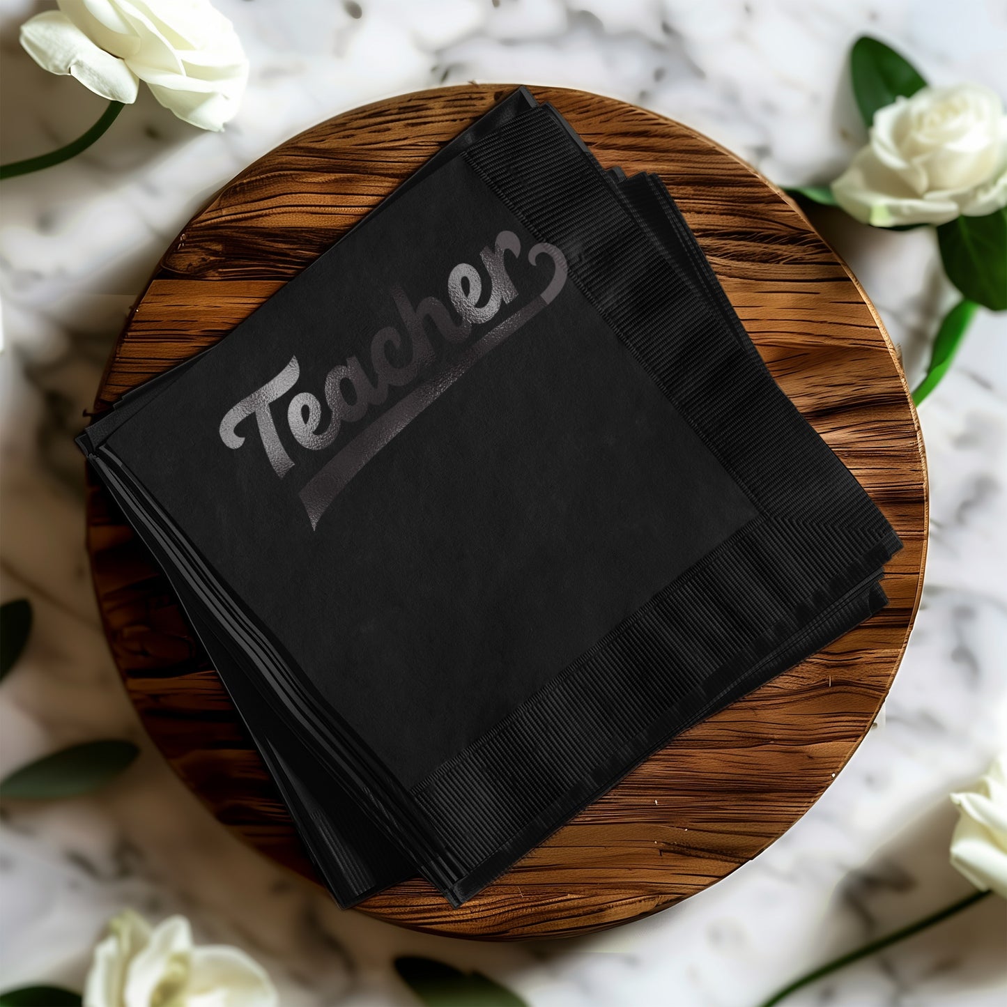 Black cocktail napkins with "Teacher" in silver lettering, stacked on a wooden board.